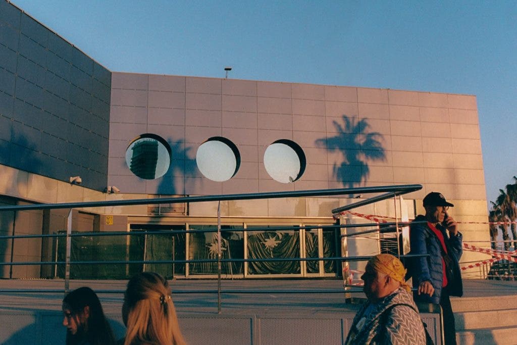 A modern building with circular windows and palm tree shadows in warm sunlight