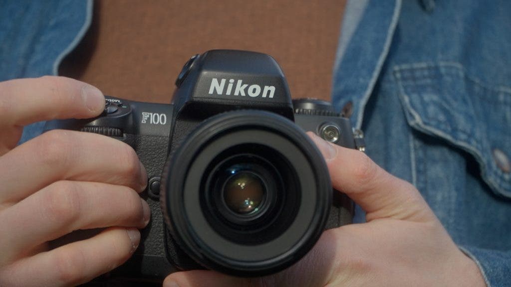 Close-up of a person's hands holding a black Nikon F100 camera