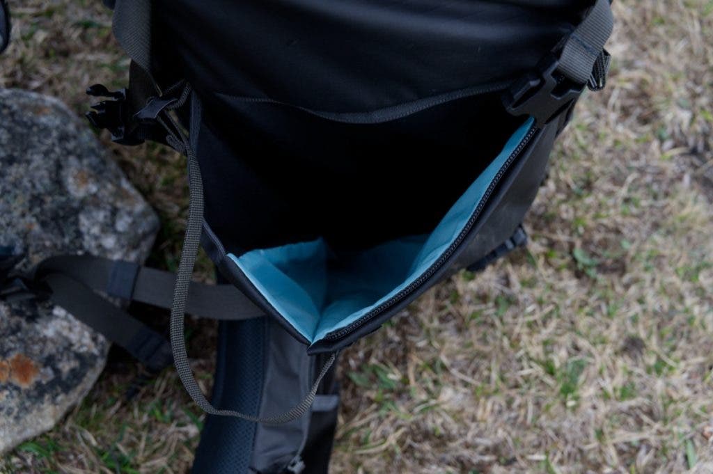 Close-up top-down view of an open side compartment on a black Shimoda Action X70 HD backpack, showing a bright teal interior lining.