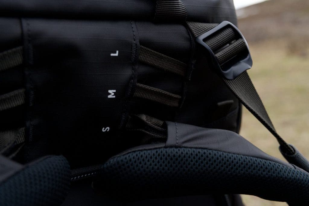 Close-up view of the adjustable harness system on a Shimoda Action X70 HD backpack, showing torso size markers labeled S, M, and L alongside shoulder straps.