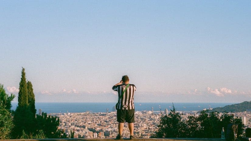 A person in a black-and-white striped jersey standing on a hilltop, looking out over a coastal city and ocean