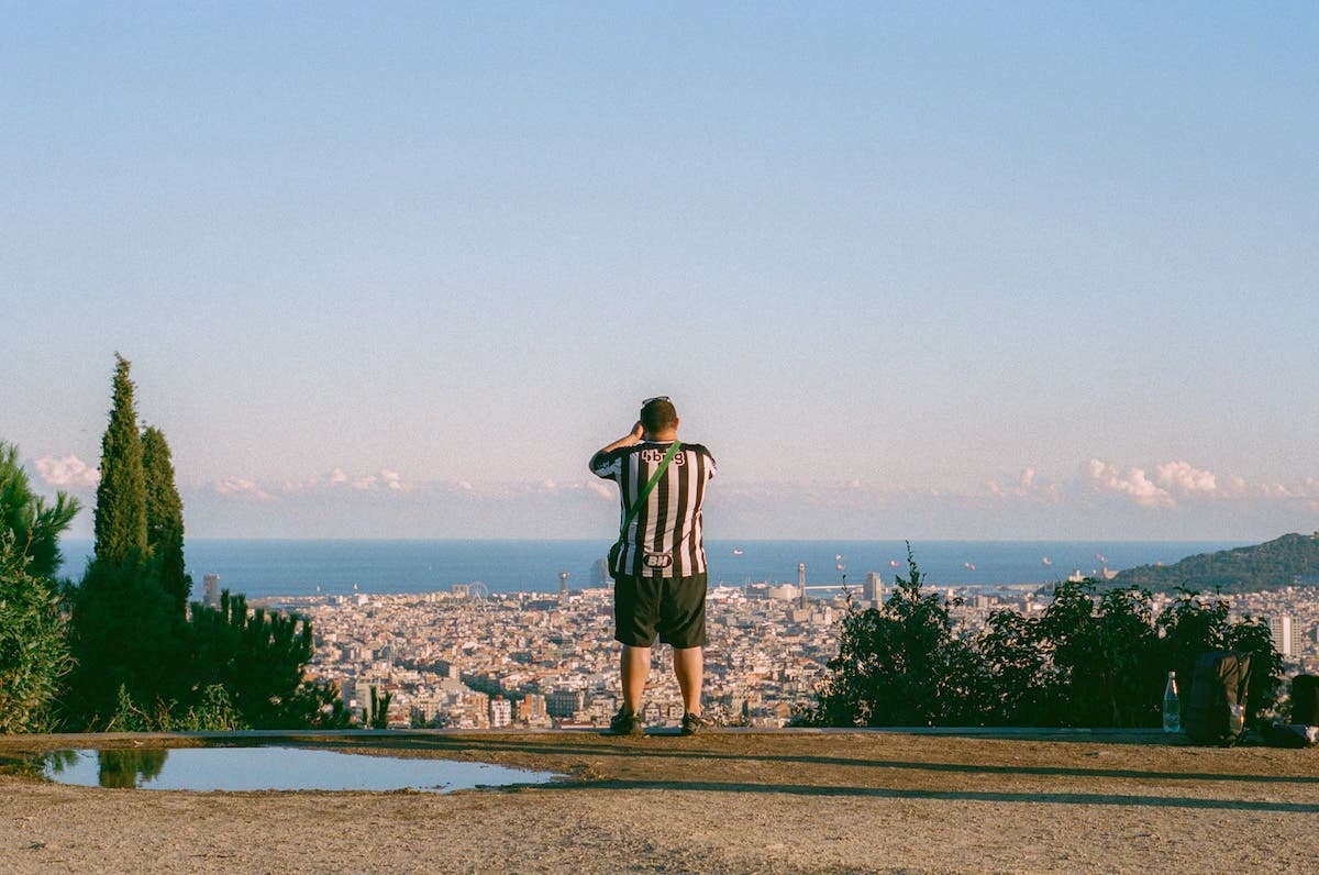 A person in a black-and-white striped jersey standing on a hilltop, looking out over a coastal city and ocean