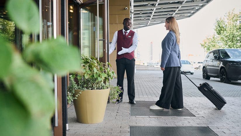 Doorman of the hotel meeting the guest and opening door for her
