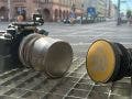 Two camera lenses resting on a metal grate with a blurred city intersection behind them; the left is a silver DZOFILM lens attached to a black camera cage, and the right is a black lens with a yellow Contax Zeiss 50 cap