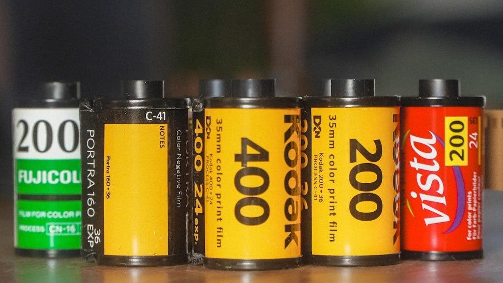 A close-up lineup of various 35mm film rolls lined up side-by-side, including Fujicolor 200, Kodak Portra 160, Kodak 400, Kodak 200, and Agfa Vista 200