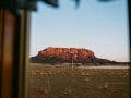 A framed view of a wide desert landscape featuring a small water tower and a red rock mesa mountain under a clear sky