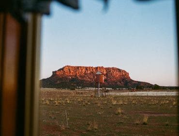 A framed view of a wide desert landscape featuring a small water tower and a red rock mesa mountain under a clear sky